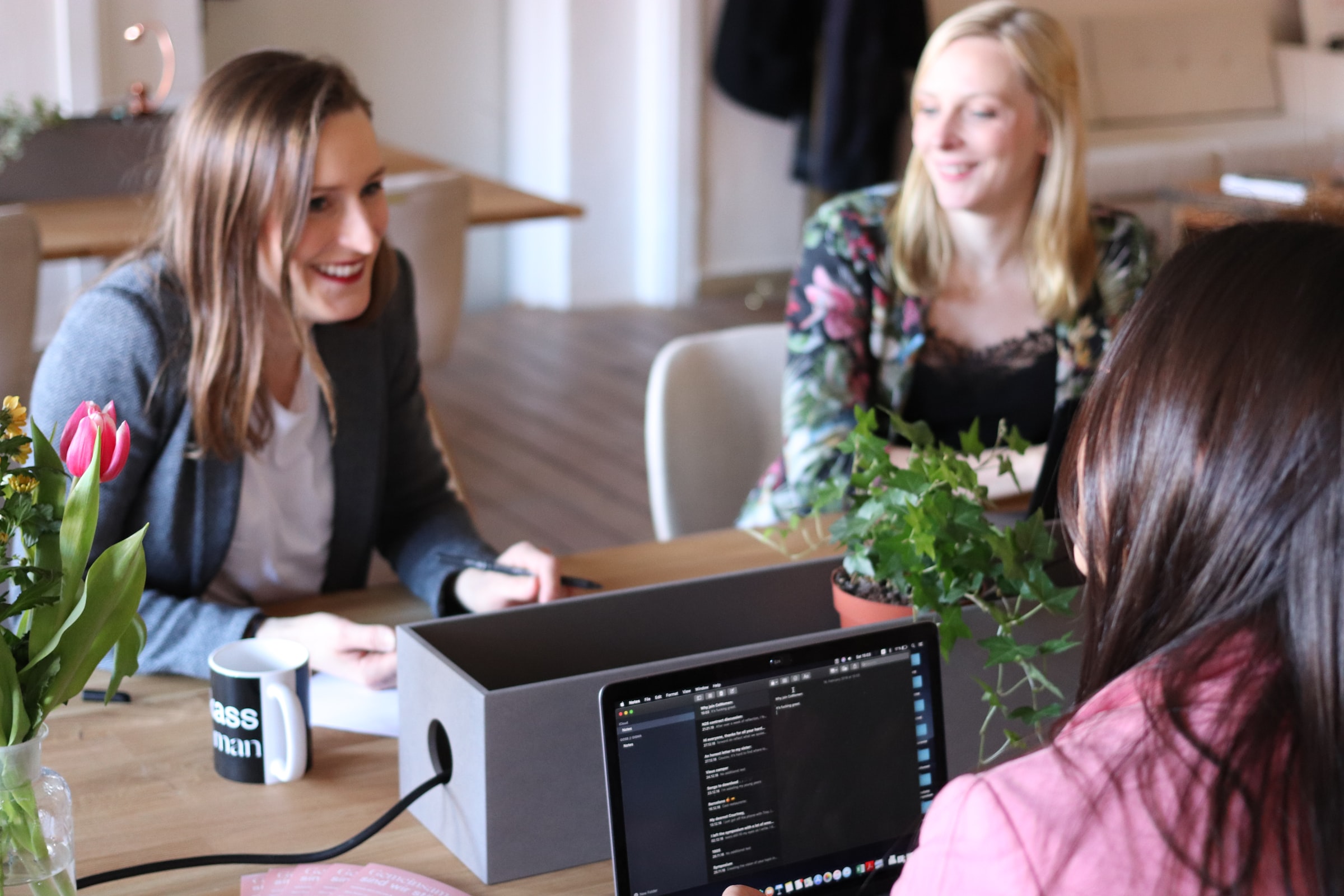 tre kvinnor sitter och pratar framför datorer